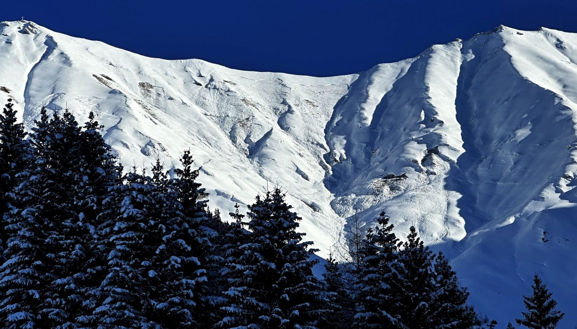 In Bildmitte erkennt man einen recht großflächigen Anriss einer Schneebrettlawine, welche sich im sehr steilen bis extrem steilen, nach Westen exponierten Kessel unterhalb der Elmer Kreuzspitze in den Östlichen Lechtaler Alpen auf rund 2400m am 25.12. spontan löste. Auslöser war vermutlich eine Gleitschneelawine, welche die entsprechend hohe Zusatzbelastung auf die Schneedecke aufbrachte (©Martin Köck, 25.12.2024).
